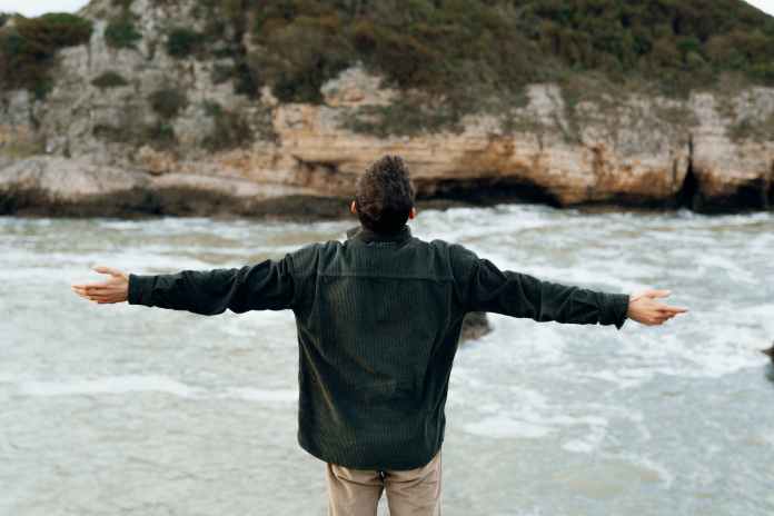 man standing on cliff by seashore