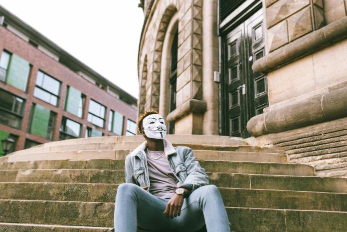 black protester in anonymous mask resting on street stairs