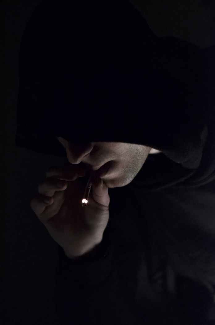 man in hoodie smoking cigarette